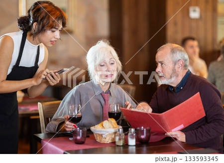 At cafe, Filipino girl waitress communicates with mature couple of customer, accepts order 133593345