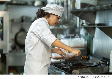 Young female cook frying ingredients in restaurant kitchen 133593402