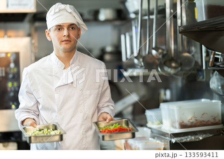 Young male chef prepares dish in restaurant kitchen Young male chef prepares dish in restaurant kitchen 133593411