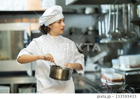 Young female chef prepares dish in restaurant kitchen 133593433