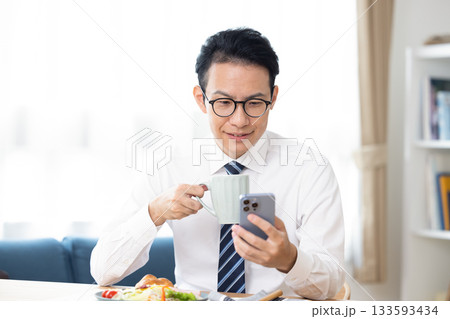 出勤前　スマホを見ながらコーヒーを飲んでいる男性 133593434