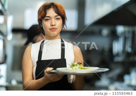 Young female waitress with prepared dish in restaurant kitchen 133593463