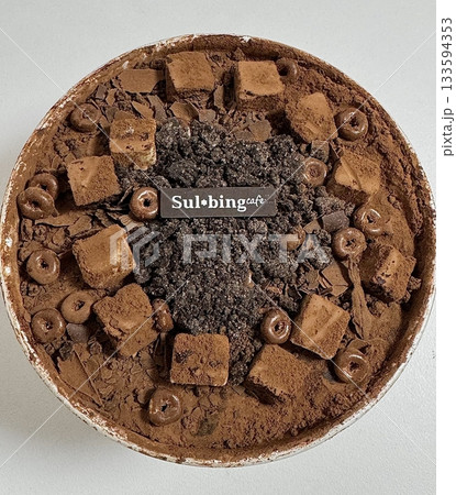 Rich and indulgent chocolate bingsu topped with chocolate syrup, brownie chunks, and chocolate shavings. A heavenly treat for chocoholics seeking a cool and creamy dessert escape. 133594353