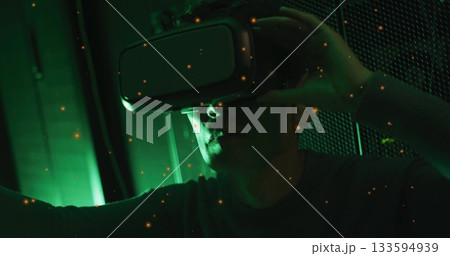 Adjusting VR headset, mature Korean man exploring virtual reality in green-lit room, with particles 133594939