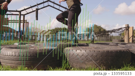 Navigating woman wearing sportswear stepping onto tire on outdoor obstacle run, with hanging ropes Navigating woman wearing sportswear stepping onto tire on outdoor obstacle run, with hanging ropes 133595133