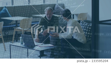 Two men in shirt and tie, green jacket coding on laptop in office lounge, with notebook 133595204