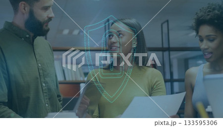 Three professionals examining documents at desk in office, with tablet, laptop and digital shield 133595306