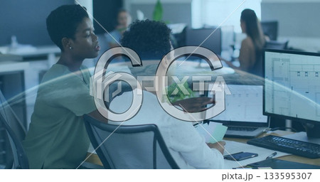 Two African American women pointing at monitor and holding documents in office, with dual monitors Two African American women pointing at monitor and holding documents in office, with dual monitors 133595307