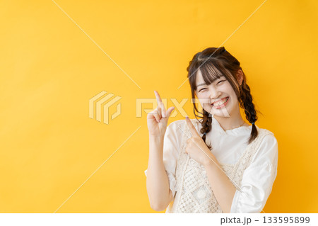 黄色い背景の前で指を差す女性 133595899
