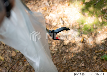 Forest cleanup in action: trash grabber tool with plastic bag in woodland setting 133596351