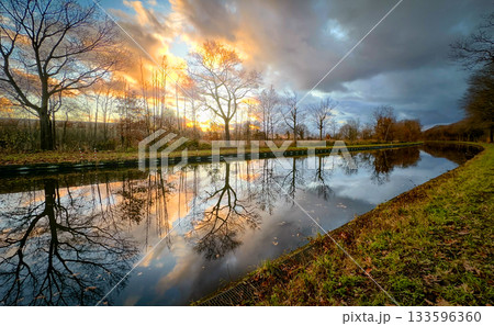 A Serene Sunset Reflection Over a Beautiful Tranquil River Landscape at Dusk, casting a warm glow A Serene Sunset Reflection Over a Beautiful Tranquil River Landscape at Dusk, casting a warm glow 133596360