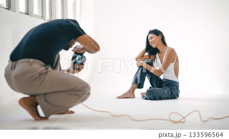 Photographer taking pictures of smiling model in photo studio Photographer taking pictures of smiling model in photo studio 133596564