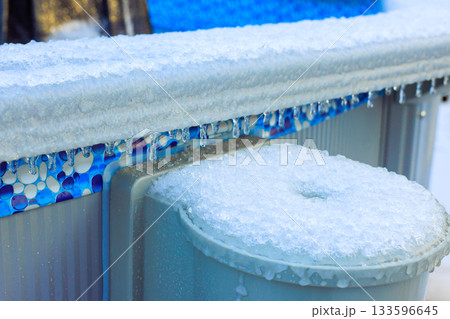 Icicles hang from pool edge as ice covers bench, reflecting winter conditions in residential area. Icicles hang from pool edge as ice covers bench, reflecting winter conditions in residential area. 133596645
