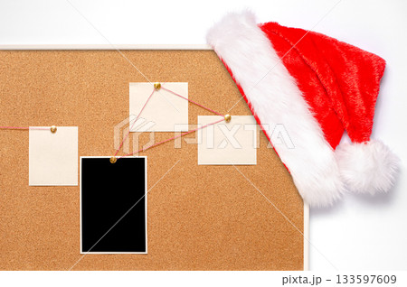 Blank paper notes and an empty photo are pinned to a cork board. Santa's hat on a cork board 133597609