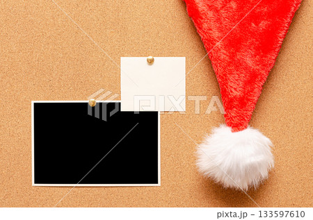 Blank paper notes and an empty photo are pinned to a cork board. Santa's hat on a cork board Blank paper notes and an empty photo are pinned to a cork board. Santa's hat on a cork board 133597610