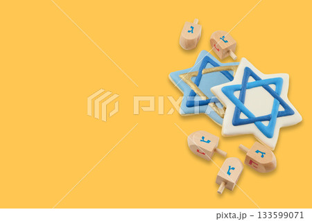 Hanukkah stars of David and wooden dreidels arranged on yellow 133599071