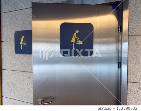 Entrance with open door to diaper changing room. Concept of changing baby diaper in public place equipped with special room and table. Symbol of mother changing baby diaper on door of changing room 133599532