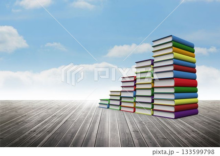 Stacks of multicolored hardcover books are rising on wooden floor under sky with clouds, copy space 133599798