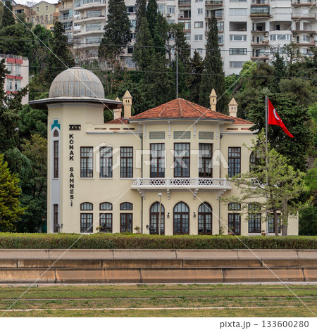 Iconic Izmir State Theatre DT Konak Sahnesi building with Turkish flag against green hills in Izmir, Turkey. 133600280