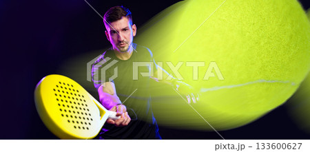 Man plays padel tennis with racket in dynamic motion on dark background 133600627