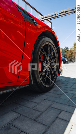 Bright red sports car parked on textured pavement under clear blue sky Bright red sports car parked on textured pavement under clear blue sky 133600688