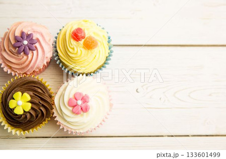 Showing four cupcakes on tabletop, showcasing pastel frosting, fondant flowers, gummies 133601499