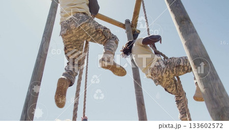 Climbing military partners navigating outdoor obstacle course, with wooden poles and climbing ropes 133602572