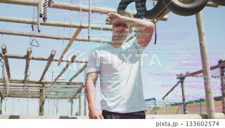 Shielding eyes fit man in athletic wear leaning back on outdoor obstacle course, with code overlay 133602574