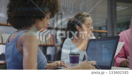 Working curly-haired woman typing on laptop in library office, with printed charts, pen, coffee cup 133602585