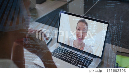 Holding smartphone viewing colleague smiling on laptop screen at home office desk, notebook and pen 133602598