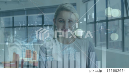 Smiling executive projecting candlestick data on industrial windows, showing line and bar charts 133602654