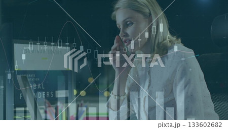 Talking businesswoman in blouse using smartphone and laptop in office at night, monitoring charts 133602682