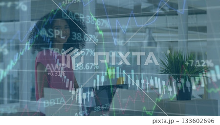 Smiling businesswoman holding laptop in modern open-plan office, with stock market chart overlays 133602696