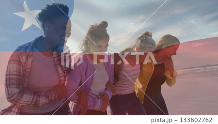 Smiling friends walking linked arm in arm along shoreline at sunset, with Liberian flag overlay 133602762