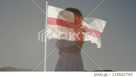 Facing woman wearing white sleeveless dress on barren hillside at dawn, with St George's cross flag Facing woman wearing white sleeveless dress on barren hillside at dawn, with St George's cross flag 133602793