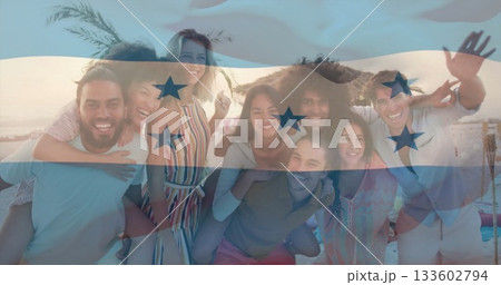 Posing group of eight friends laughing on sandy beach at sunset under straw umbrella, palm fronds 133602794