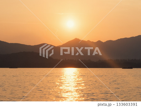 Scenic landscape of West Lake, Hangzhou, during golden hour with sun rays shining through the distant mountains Scenic landscape of West Lake, Hangzhou, during golden hour with sun rays shining through the distant mountains 133603391