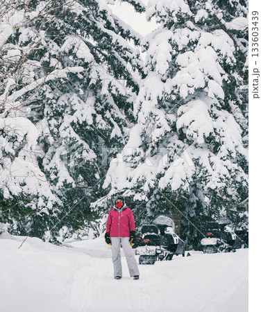 Young woman dressed in bright pink stands joyfully amidst towering snow-covered trees in a serene winter landscape. 133603439