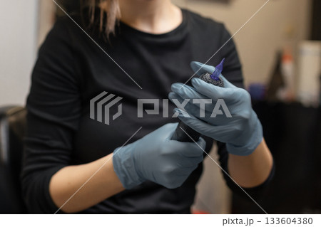 tattoo artist in gloves preparing a tattoo machine, attaching a sterile needle cartridge before a session in a professional studio. tattoo artist in gloves preparing a tattoo machine, attaching a sterile needle cartridge before a session in a professional studio. 133604380