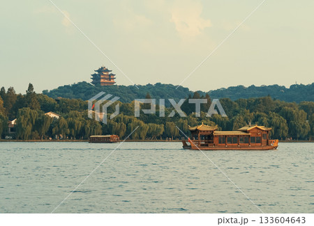 Wooden tourist boats navigate west lake in Hangzhou, China near pagoda temple on hill at dusk Wooden tourist boats navigate west lake in Hangzhou, China near pagoda temple on hill at dusk 133604643