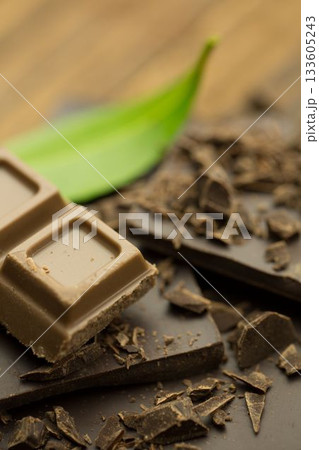 milk chocolate square is resting on dark chocolate fragments beside green leaf in macro photography 133605243