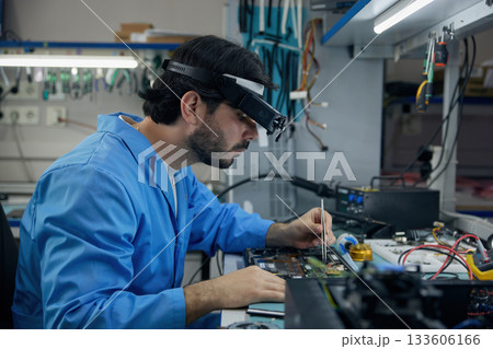 Technician man soldering technician dressed in a blue lab coat is diligently repairing a laptop Technician man soldering technician dressed in a blue lab coat is diligently repairing a laptop 133606166