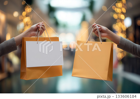 Shopping bags with single-color banner panels held by hands in softly blurred mall scene 133606184
