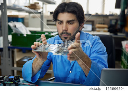 A man worker is wearing a blue shirt holding a motherboard in his hands A man worker is wearing a blue shirt holding a motherboard in his hands 133606204