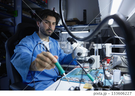 A technician skillfully repairs electronic components with precision tool 133606227