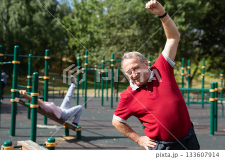 Aged man practicing gymnastics in open-air sports area Aged man practicing gymnastics in open-air sports area 133607914