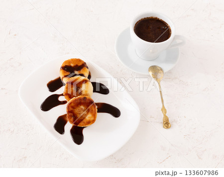 Curd fritters with chocolate on the porcelain plate and a cup of coffee. 133607986