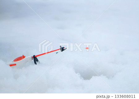 Red fishing float on rod bobbing near ice fishing hole during winter fishing. 133608011