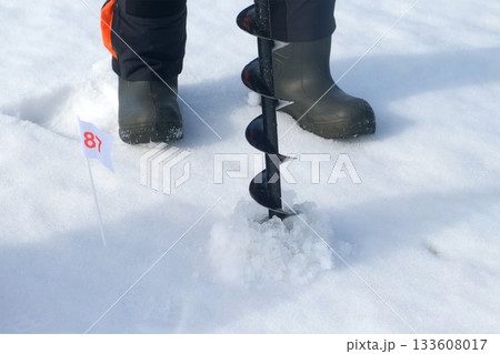 Ice fisherman drilling hole with ice auger preparing to catch fish in winter. Ice fisherman drilling hole with ice auger preparing to catch fish in winter. 133608017