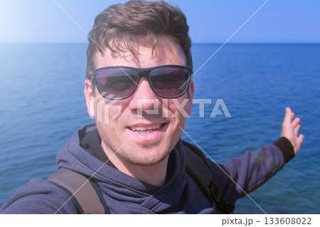 Man video chats selfie smartphone on sea beach waves hand greets and smiles. Man video chats selfie smartphone on sea beach waves hand greets and smiles. 133608022